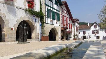 A traditional European town square with half-timbered buildings, a statue, and a narrow water channel.