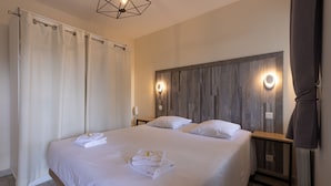 Une chambre d’hôtel avec un grand lit, deux tables de chevet, une tête de lit en bois et un luminaire moderne.