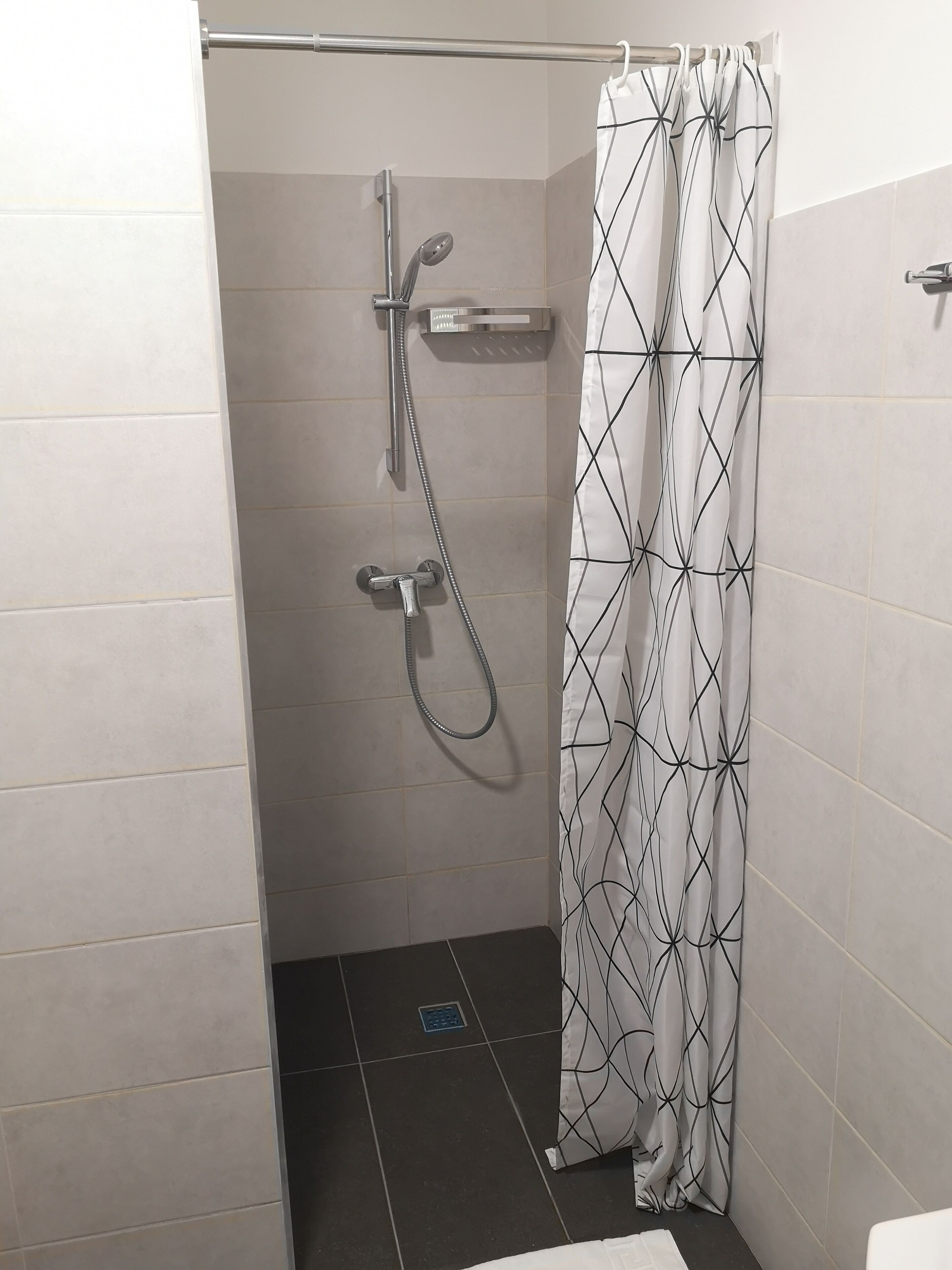 A shower area with a handheld showerhead, a wall-mounted faucet, and a patterned shower curtain.