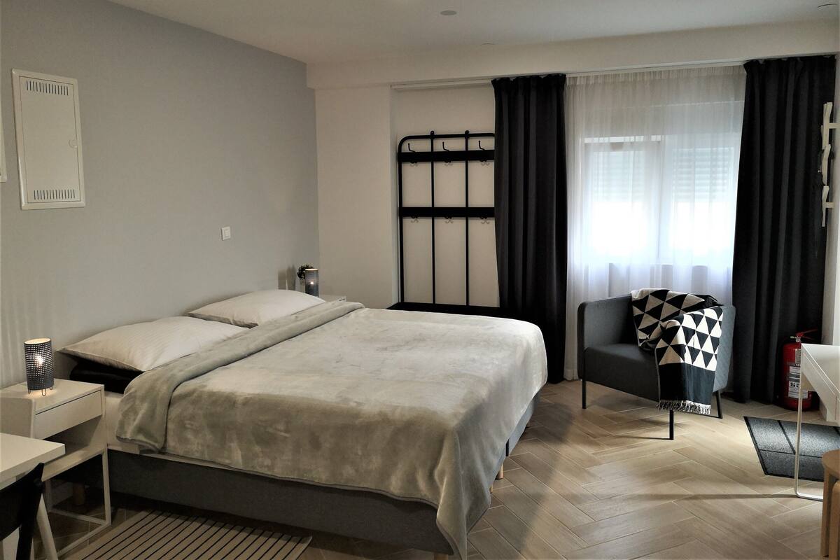 Ein modernes Schlafzimmer mit Bett, Nachttischen, einem Sessel und einem Fenster mit Vorhängen.