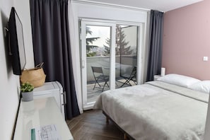 Ett hotellrum med en säng, ett skrivbord med en dator, en stol och utsikt över staden genom en skjutdörr.