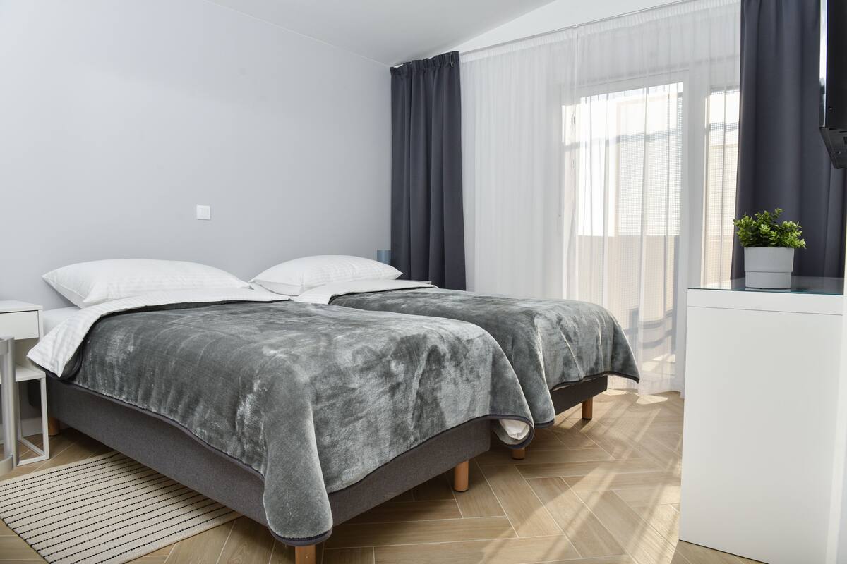 Ein modernes Schlafzimmer mit zwei Betten, einem Nachttisch, einem kleinen Schreibtisch und einer Topfpflanze.
