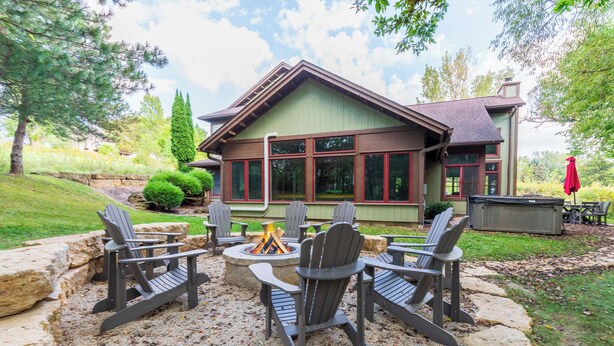 Een huis met een vuurkuil in het midden, omringd door Adirondack stoelen.