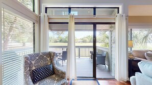 Una habitación con puerta corredera de vidrio que da a una terraza exterior, un sillón estampado y un sofá.