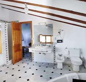 Een badkamer met een wastafel, toilet en bidet, met betegelde vloer en houten balken in het plafond.