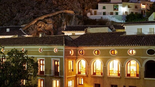 Un edificio tradicional con varias ventanas y un patio interior, rodeado de terreno pedregoso.