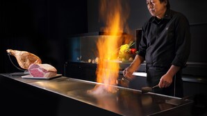 A chef preparing food on a hot griddle with a large piece of meat and vegetables.