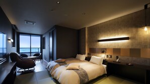 A modern hotel bedroom with a large bed, a desk, and a chair. There is a view of the city from the window.