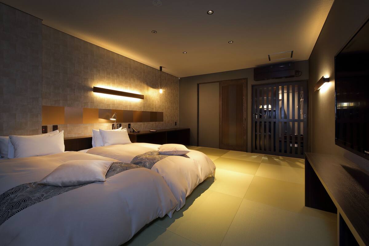 A modern hotel room with a large bed, bedside tables, a TV, and a sliding door closet.