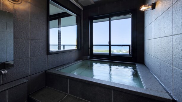 A modern bathroom with a large bathtub, a window with a view, and a wall-mounted light fixture.
