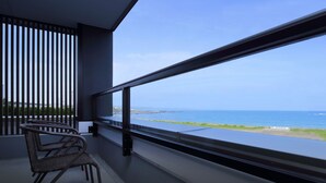 A balcony with a view of the sea, featuring a wicker chair and a table.