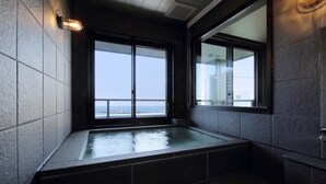 A modern bathroom with a large bathtub, a view of the ocean, and a stone-tiled wall.