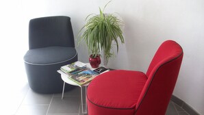Una habitación moderna con una silla roja, una silla azul oscuro y una pequeña mesa con revistas.