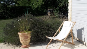 Un jardín con una maceta de terracota grande y una silla de playa de madera.