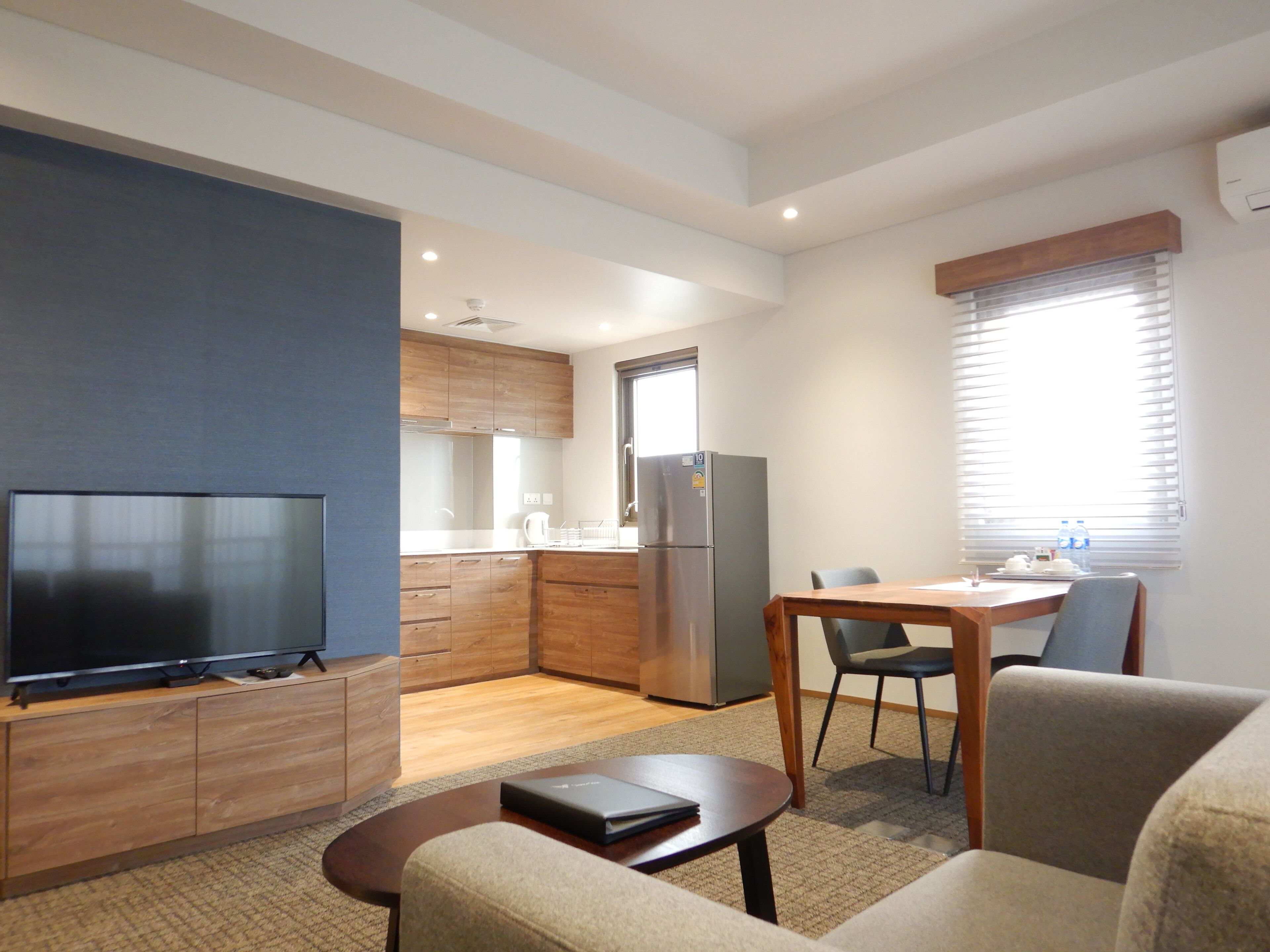 A modern living room with a flat-screen TV, a sofa, a coffee table, and a dining area with a table and chairs.