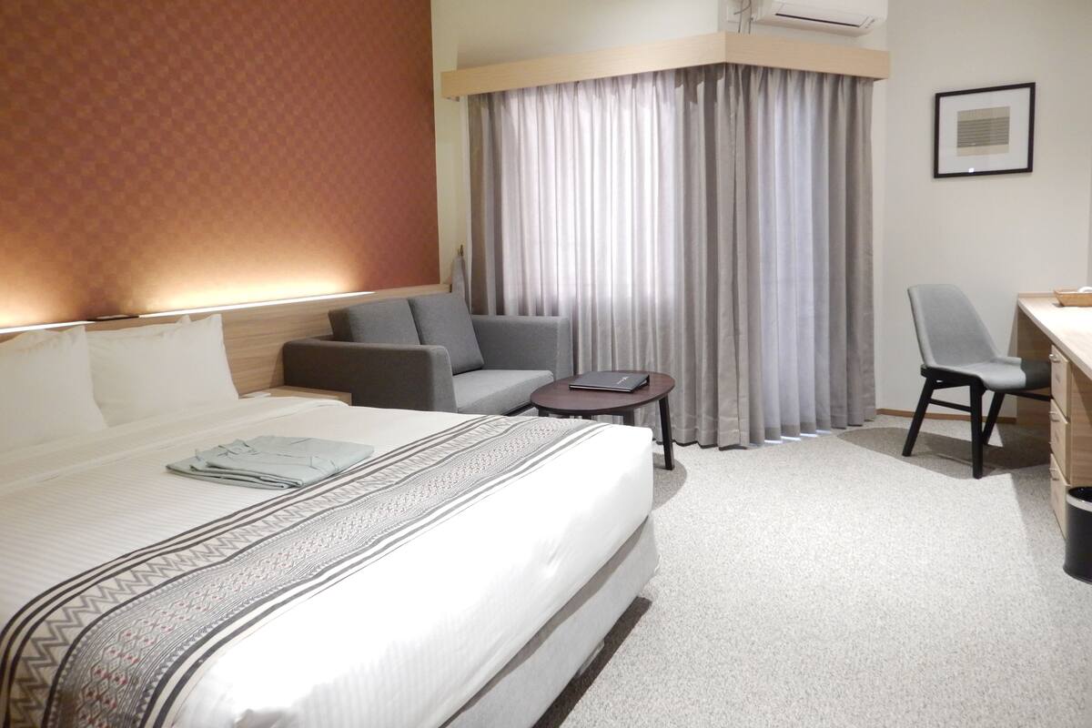 A hotel room with a large bed, a sofa, a desk, and a chair.