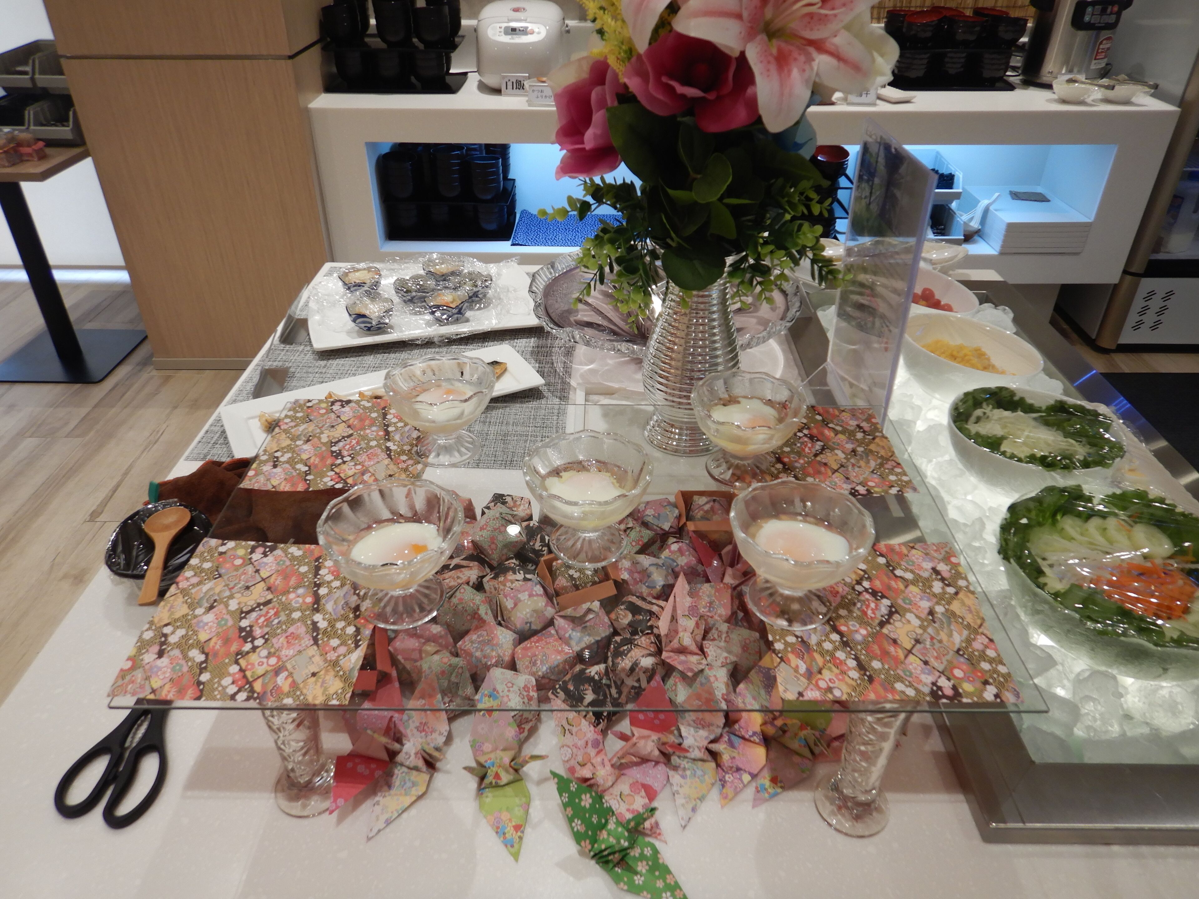 Een tafel met origami-decoraties, een vaas met bloemen en diverse etenswaren.