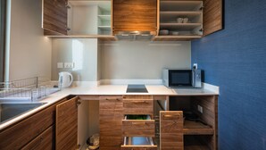 A compact kitchen with wooden cabinetry, a microwave, and a kettle. - Wishton Hotel Yangon (Yangon)