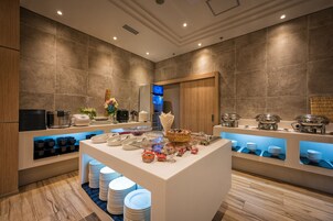 Una moderna presentación de bufé con una isla central, estaciones de bufé y una variedad de recipientes para alimentos y bebidas.
