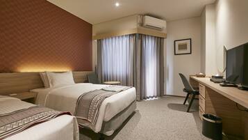 A hotel room with two beds, a desk with a computer, a TV, and an air conditioning unit.