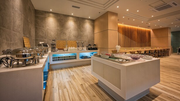 A modern hotel lobby with a buffet area, wooden paneling, and a seating area with tables and chairs. - Wishton Hotel Yangon (Yangon)