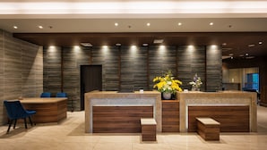 A modern reception area with a wooden reception desk, blue chairs, and a vase of yellow flowers. - Wishton Hotel Yangon (Yangon)
