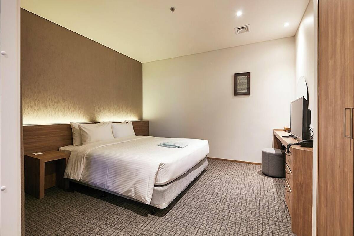 A hotel room with a bed, bedside table, TV, and a small desk with a chair.