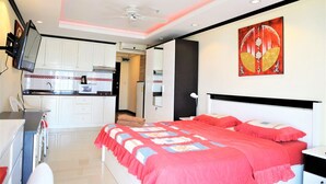 A bedroom with a large bed, a kitchenette, and a ceiling fan. - Sea Views at Jomtien Beach (Pattaya)