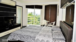 Ein modernes Schlafzimmer mit einem großen Bett, einem Fernseher, einem Schreibtisch und einem Balkon mit Aussicht.