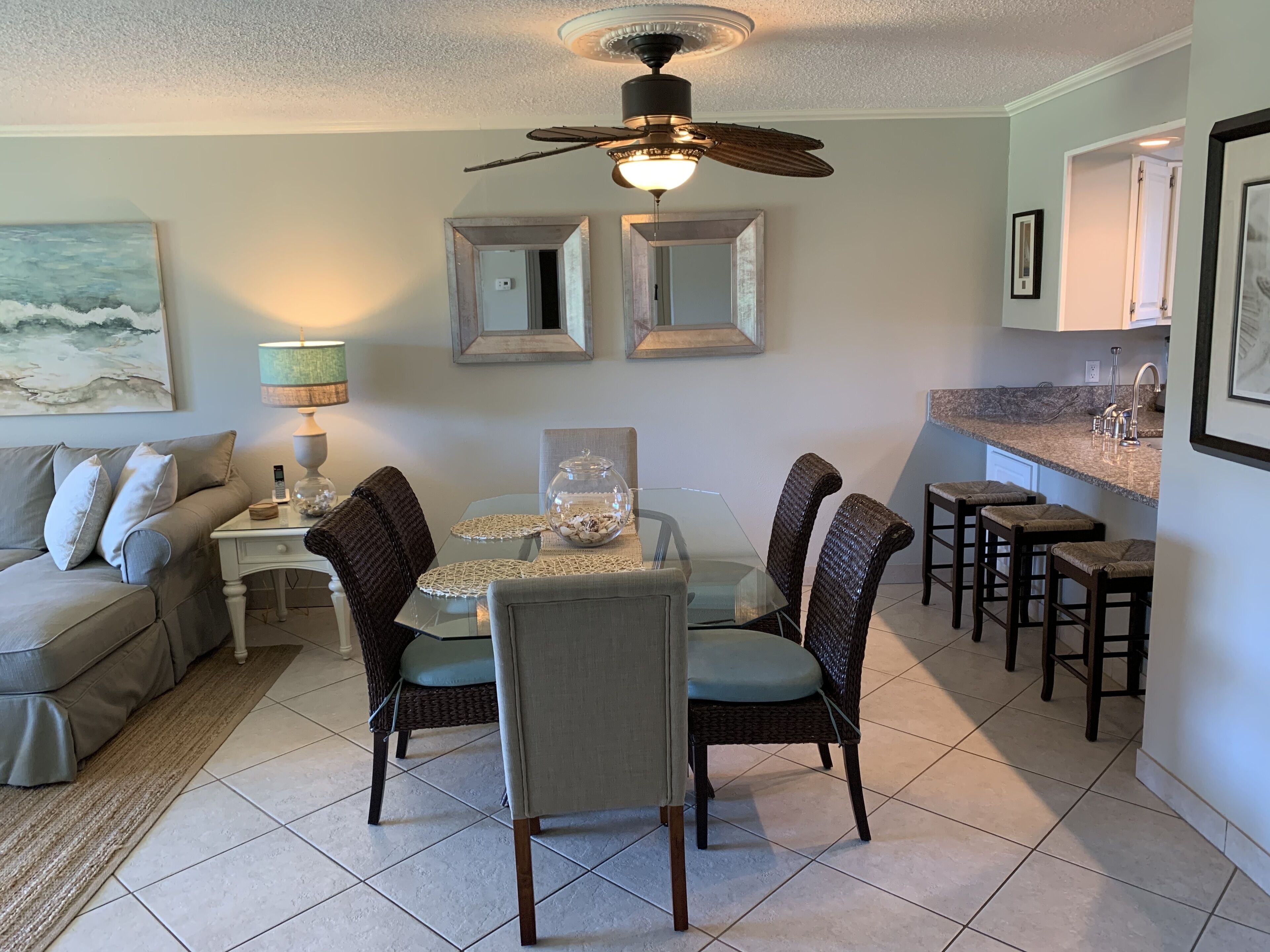 A dining area with a glass table, wicker chairs, and a ceiling fan.