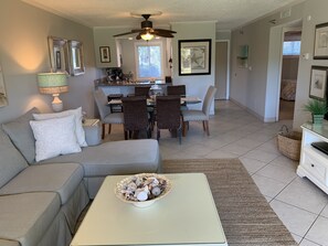 A living room with a sofa, a coffee table with decorative items, a dining area with chairs and a table, and a ceiling fan. - Great Views + Easy Access! Ground Floor Beach Escape – Islander 116 (Destin)