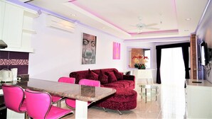 Un salon moderne avec un canapé rouge, des fauteuils roses, une table basse en verre et un ventilateur de plafond.