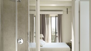 A modern hotel room with a glass shower enclosure, a bed with a view of the outdoors, and a small bedside table with a lamp. - Luna del Raccolto (Valderice)