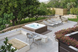 A patio area with a hot tub, lounge chairs, and a table with chairs.
