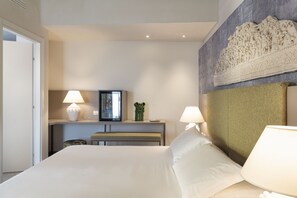 A hotel room with a large bed, two bedside lamps, a small table with a lamp, a decorative wall piece, and a window with blinds.