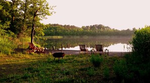 Terraza junto al lago con sillas de madera y una parrilla.