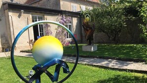 Een sculptuur in een tuin, met een huis op de achtergrond.