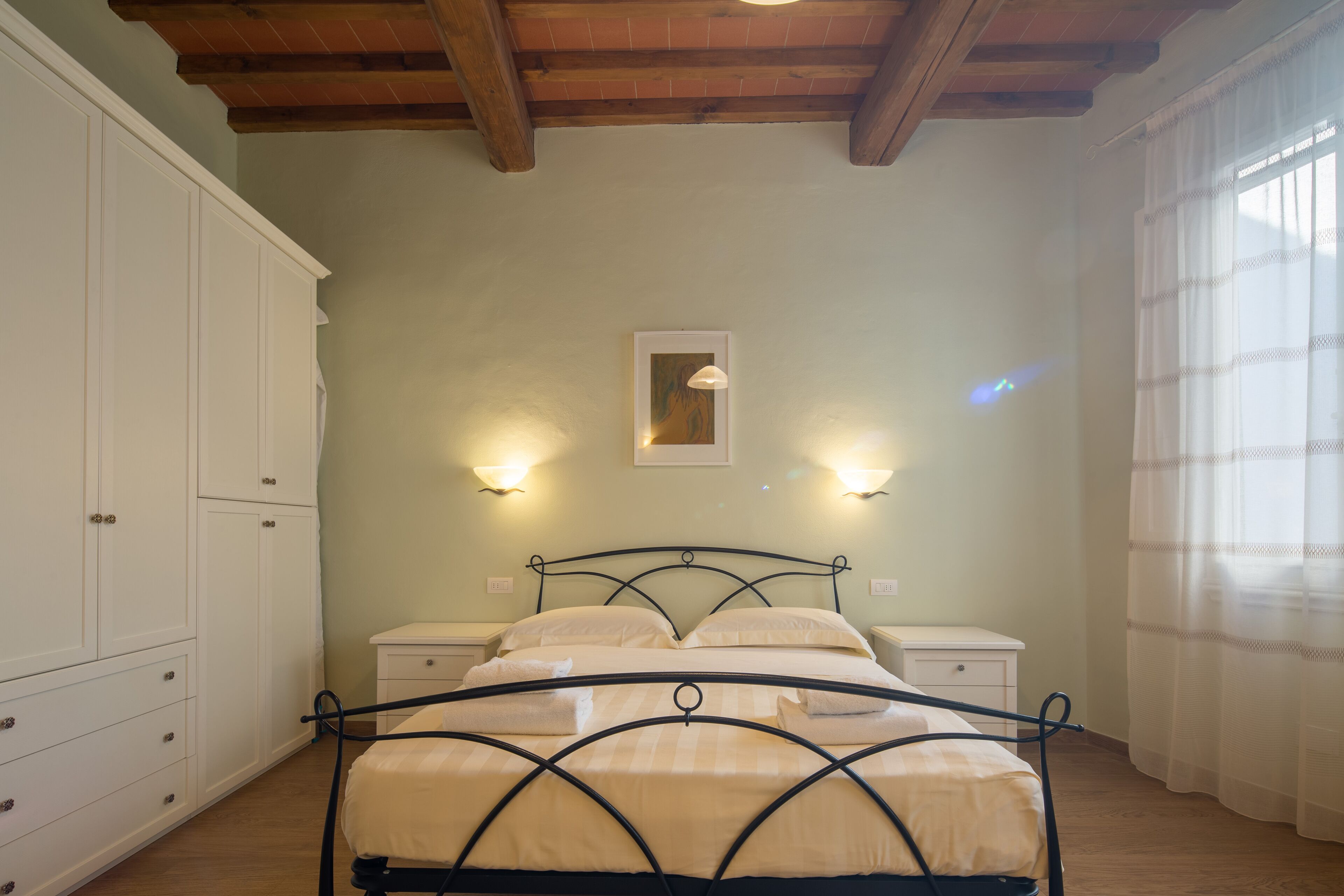 A bedroom with a bed, nightstands, a wardrobe, and a ceiling with exposed beams.