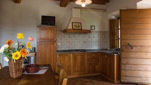 Una cocina con armarios de madera, salpicadero de azulejos, estufa y un televisor en un estante.
