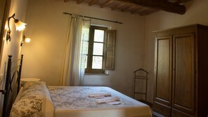 Un dormitorio con cama, armario de madera, ventana con cortinas e iluminación en la pared.
