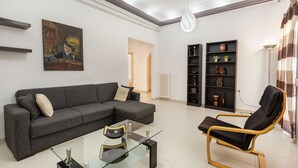 A modern living room with a grey sectional sofa, a glass coffee table, a black lounge chair, and a bookshelf with decorative items. - Mirsini's Apartment in Chania Center (Chania)