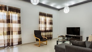 A modern living room with a sofa, a black chair, a glass coffee table, and a TV. - Mirsini's Apartment in Chania Center (Chania)