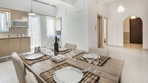 A modern dining area with a wooden table set for four, surrounded by chairs. A kitchen area is visible to the left with a microwave and cabinets. - Mirsini's Apartment in Chania Center (Chania)