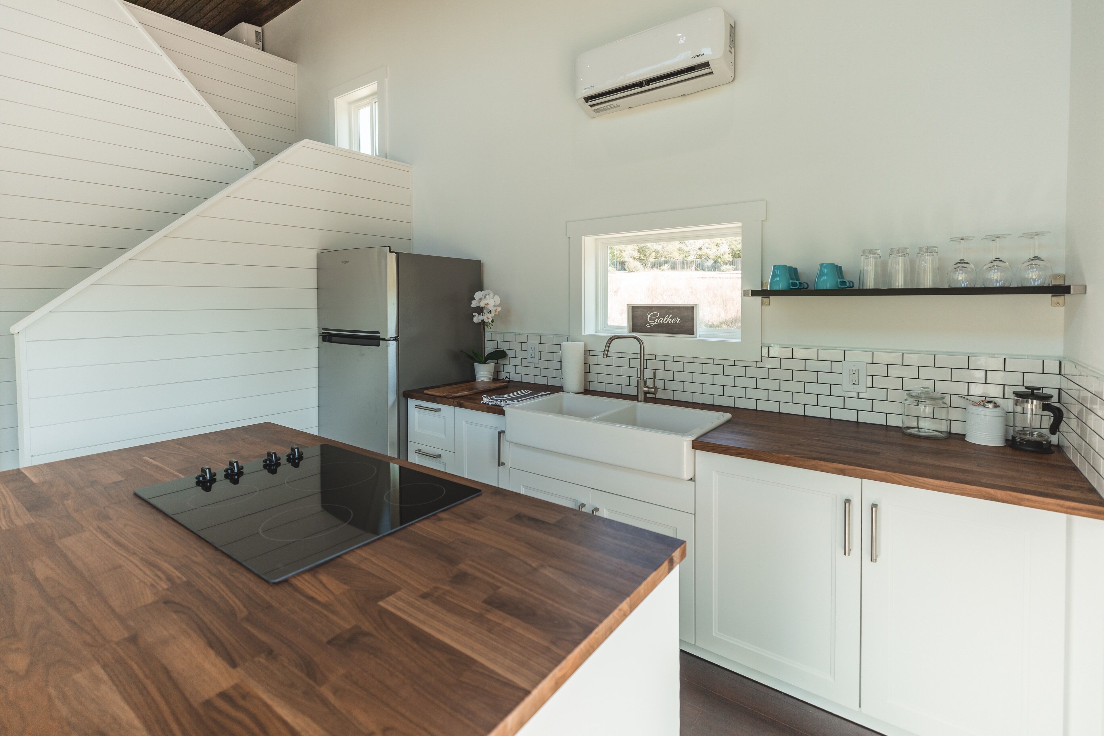 A modern kitchen with a wooden countertop, white cabinets, a built-in stove, and a window above the sink.