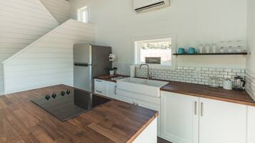 A modern kitchen with a wooden countertop, white cabinets, a built-in stove, and a window above the sink.