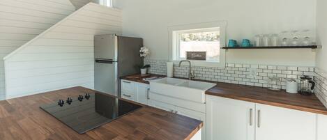 Una cocina moderna con encimera de madera, armarios blancos, estufa integrada y ventana sobre el lavabo.
