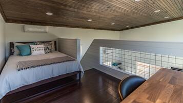 Un dormitorio con techo de madera, una cama con almohadas estampadas, una mesita de noche y vistas a través de una ventana con diseño de celosía.