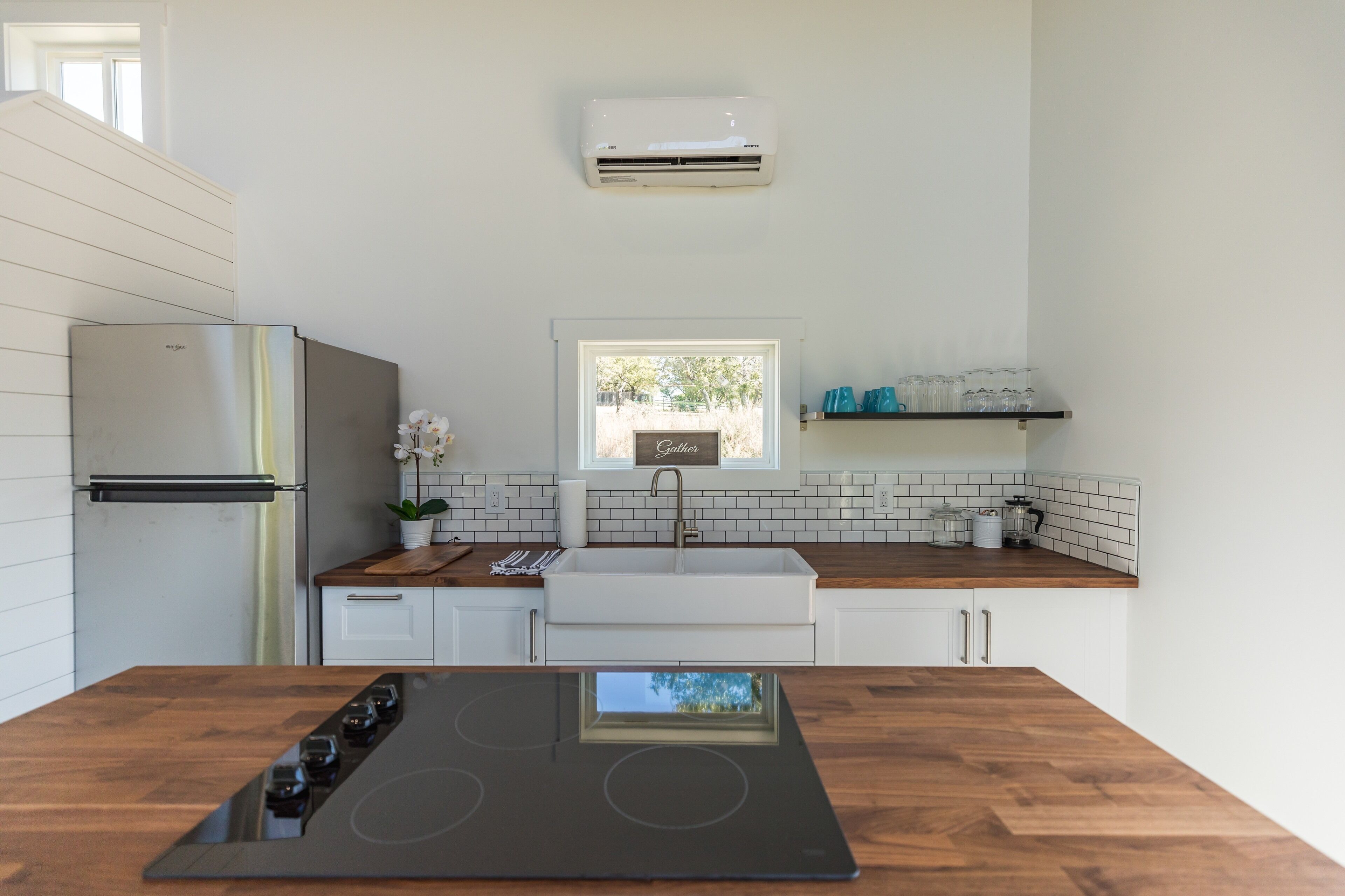 Una cocina moderna con estufa integrada, refrigerador, ventana con vistas y repisas con vasos.
