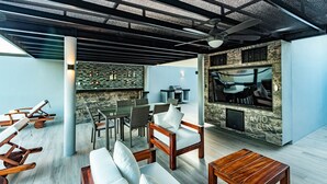 Een moderne buitenlounge met zitplaatsen, een bar en een televisiescherm.