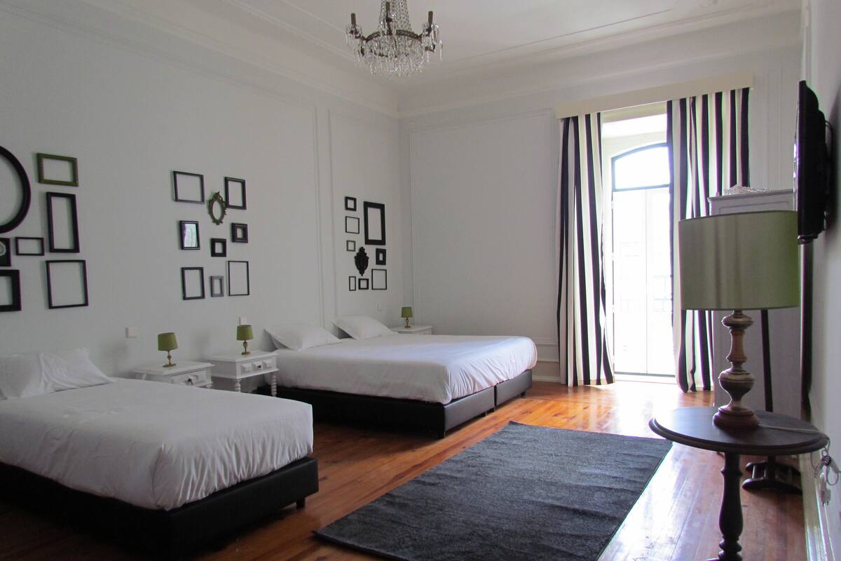 Habitación de hotel con dos camas, un candelabro, un televisor y una ventana con cortinas a rayas.